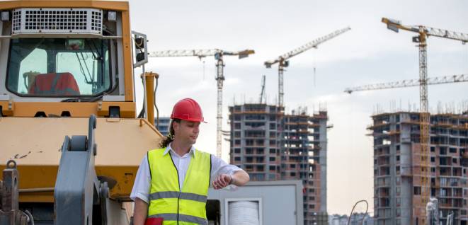 Construction site engineer stands next to a bulldozer in front of the construction site