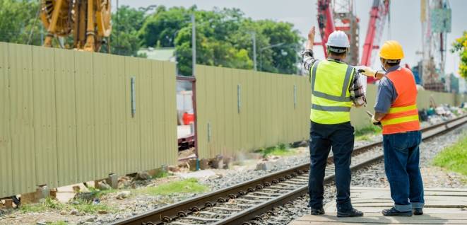 Engineers overseeing track works at a railway construction site. Professionals in safety gear point towards urban infrastructure development
