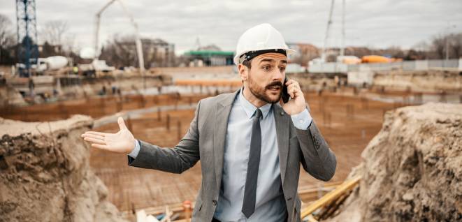 An angry architect is speaking on the phone with constructors and arguing about delay.