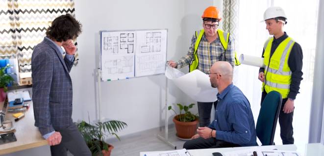 A team of builders, an engineer and an architect are discussing drawings and plans for the construction of a modern business center