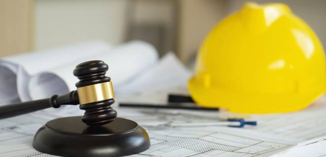 Labor and Construction law concept. judge gavel on building blueprint plans with a yellow safety helmet in the background