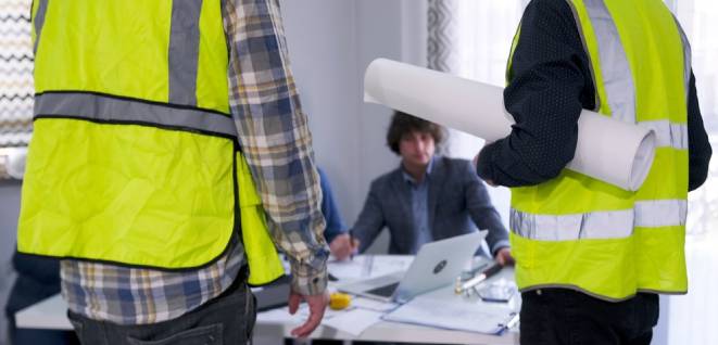 A foreman and a worker in green vests with drawings in their hands stand at the desk of the head of the architectural bureau and ask for a raise in their salaries.